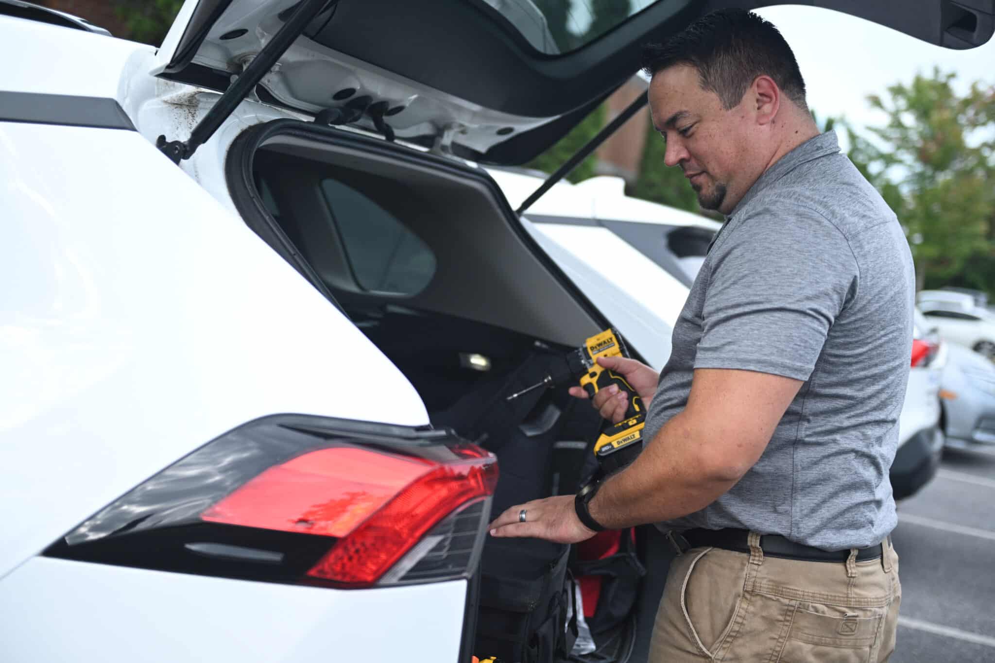 A guys holding a drill behind his car